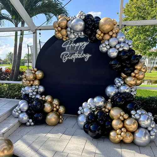 Black, gold and silver organic balloon garland arch birthday decoration set up outdoors on a patio with Happy Birthday neon sign in Indore