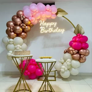Rose gold and pink circular balloon arch birthday decoration with two gold dessert tables and Happy Birthday neon sign in Indore