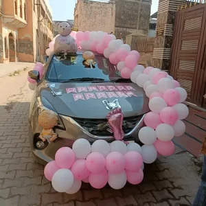 Pink and white balloon arch with Welcome Baby banner, baby doll and butterfly decoration on car in Indore