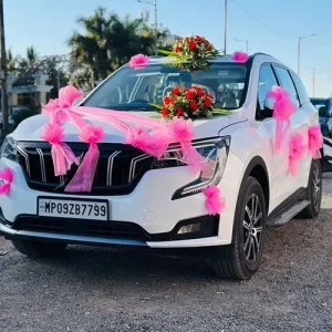 Pink net bow and red rose flower bouquet wedding car decoration on white Mahindra XUV700 in Indore
