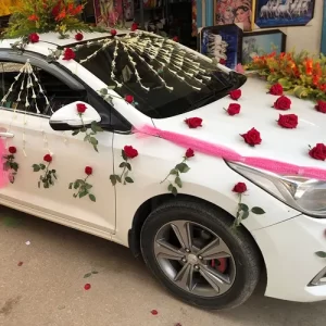 Red roses, string garland and pink tulle wedding car decoration on white Hyundai Verna sedan in Indore